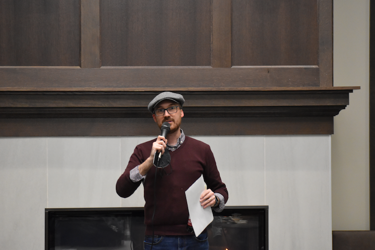 Patrick Thomas Henry speaking into mic while standing in front of a fireplace