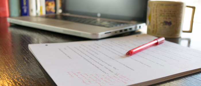 Desk with manuscript and red pen, laptop, and coffee cup