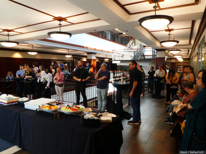 People standing in front of buffet table and listening to a speaker